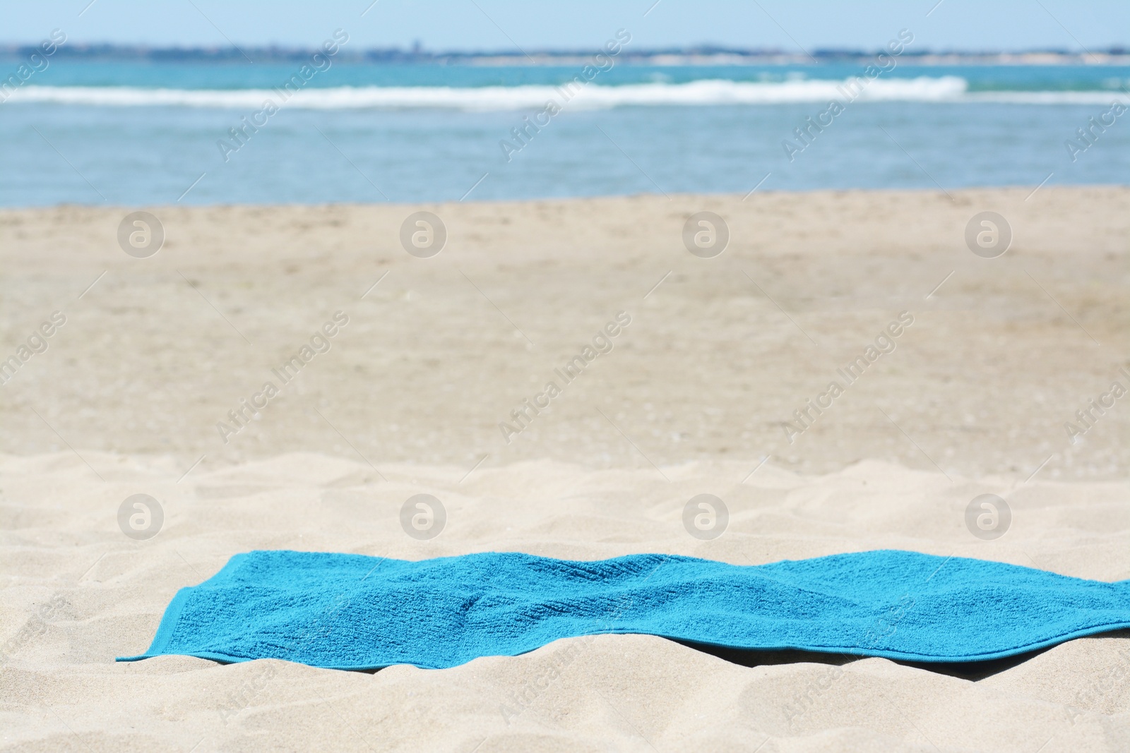 Photo of Soft blue towel on sandy beach near sea, space for text