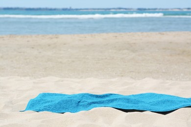 Soft blue towel on sandy beach near sea, space for text