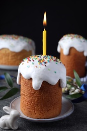 Photo of Traditional Easter cakes and one with burning candle on grey table against black background