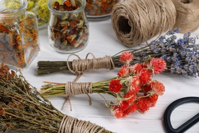 Bunches of dry flowers, different medicinal herbs and spools on white wooden table