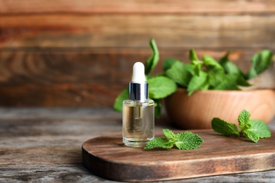 Photo of Essential oil in glass bottle and mint on wooden table. Space for text