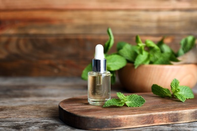 Essential oil in glass bottle and mint on wooden table. Space for text