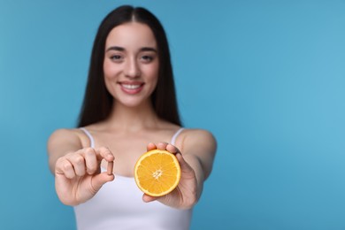 Beautiful young woman with vitamin pill and piece of orange on light blue background, selective focus. Space for text