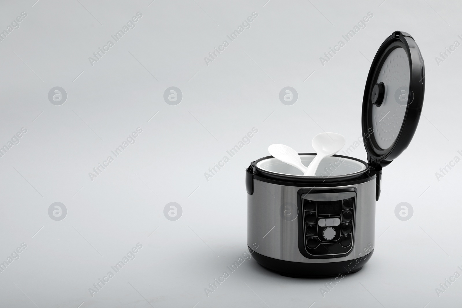 Photo of Modern electric multi cooker with spoon and ladle on grey background. Space for text