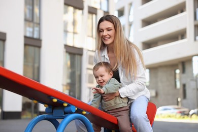 Photo of Happy nanny with cute little boy on seesaw outdoors