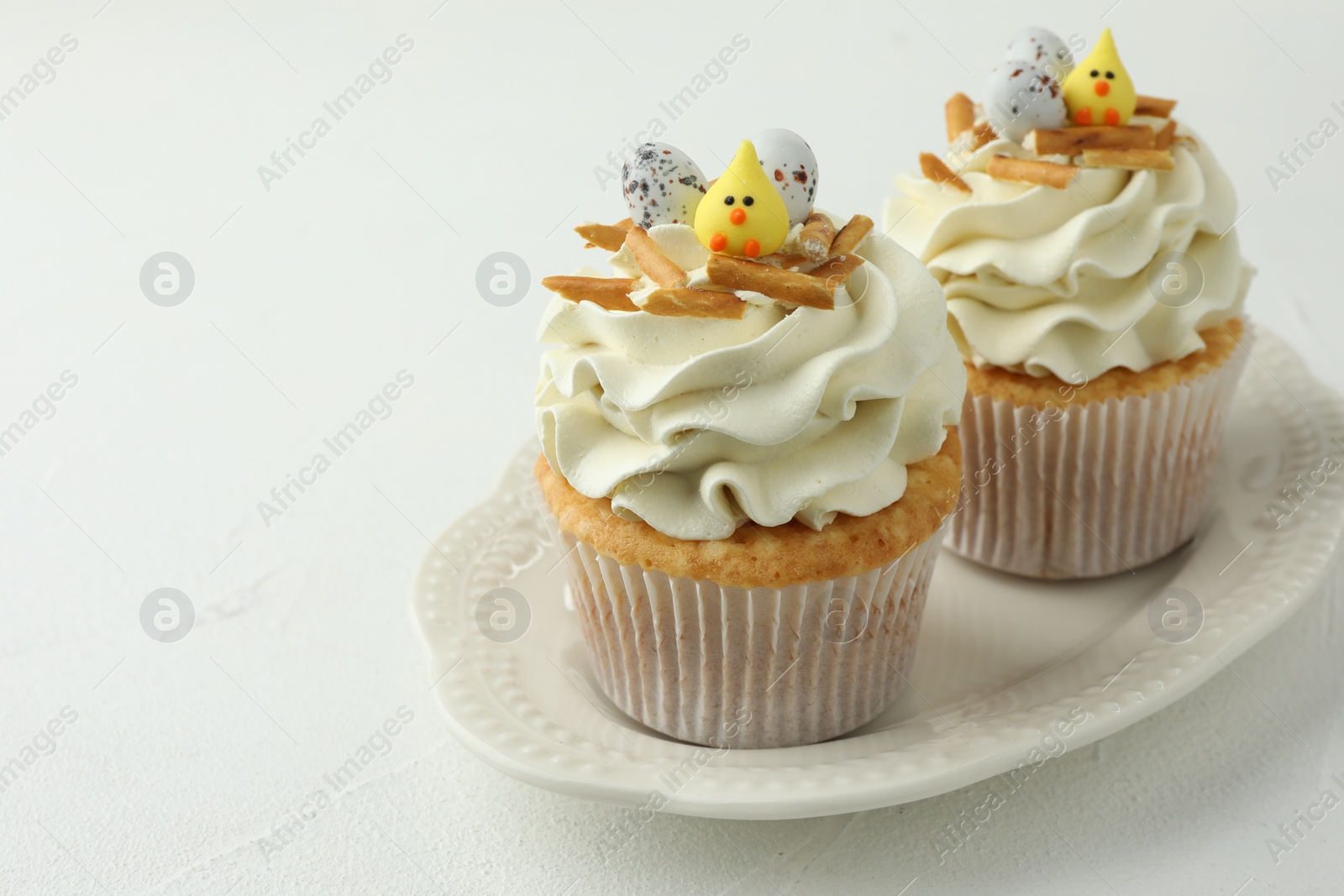 Photo of Tasty Easter cupcakes with vanilla cream on white table, closeup. Space for text