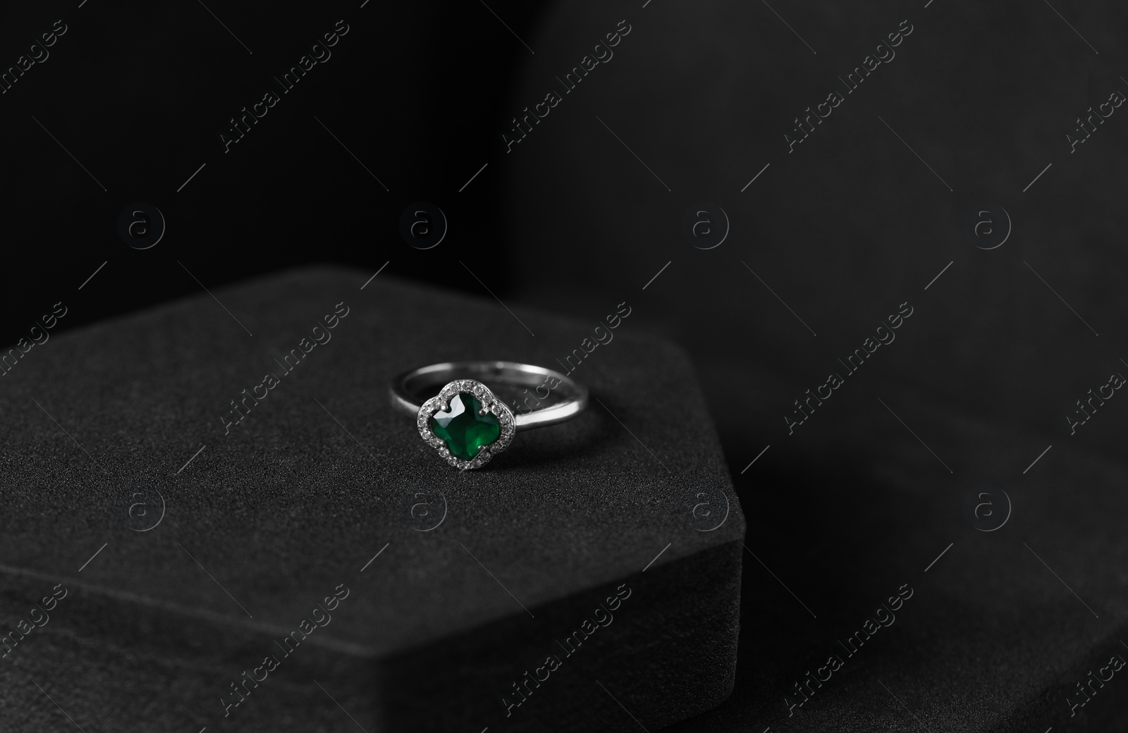 Photo of Beautiful ring with green gemstone on black podium, space for text. Luxury jewelry