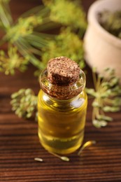 Bottle of essential oil and fresh dill on wooden table, closeup