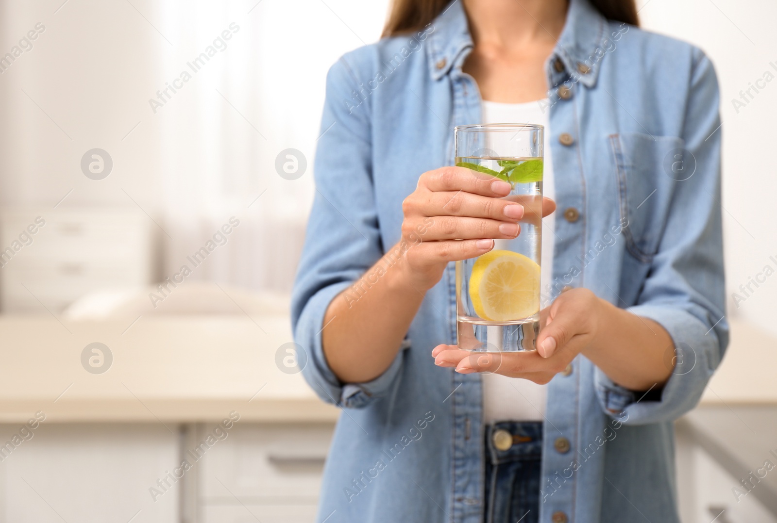 Photo of Young woman with glass of lemon water at home, closeup. Space for text