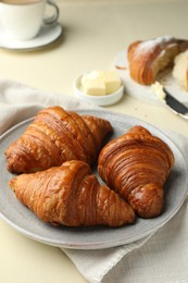 Photo of Plate with tasty croissants on beige table, closeup