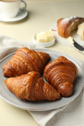 Plate with tasty croissants on beige table, closeup