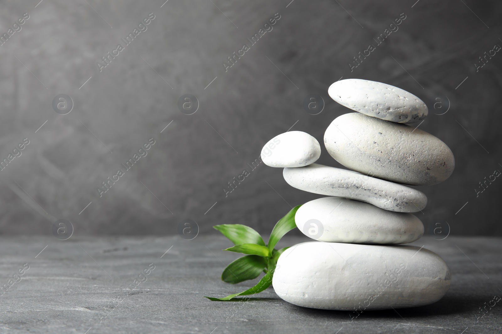 Photo of Stack of zen stones and bamboo leaves on table against grey background. Space for text