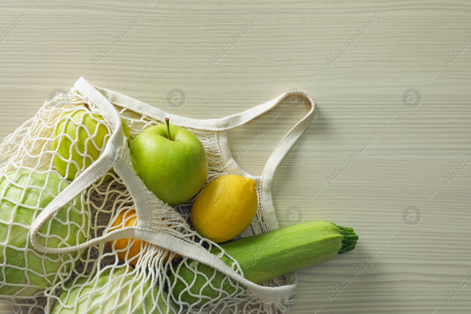 Photo of Net bag with vegetables and fruits on wooden table, top view