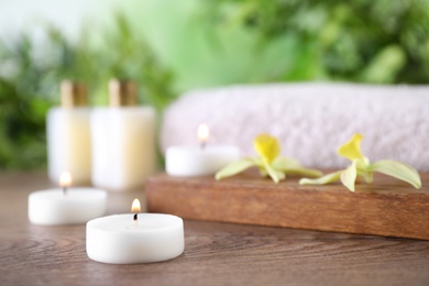 Photo of Composition with burning candles and flowers on wooden table against blurred background, space for text. Spa concept