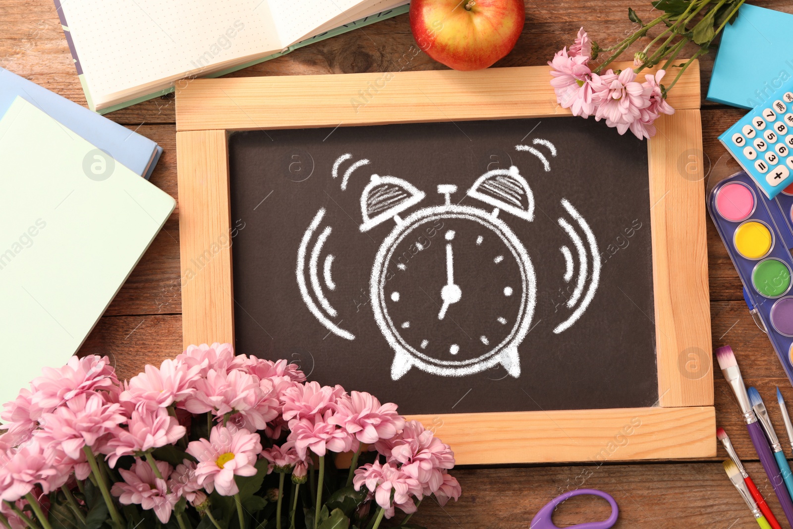 Image of Small blackboard with drawn alarm clock, flowers and different stationery on wooden table, flat lay. Time to school