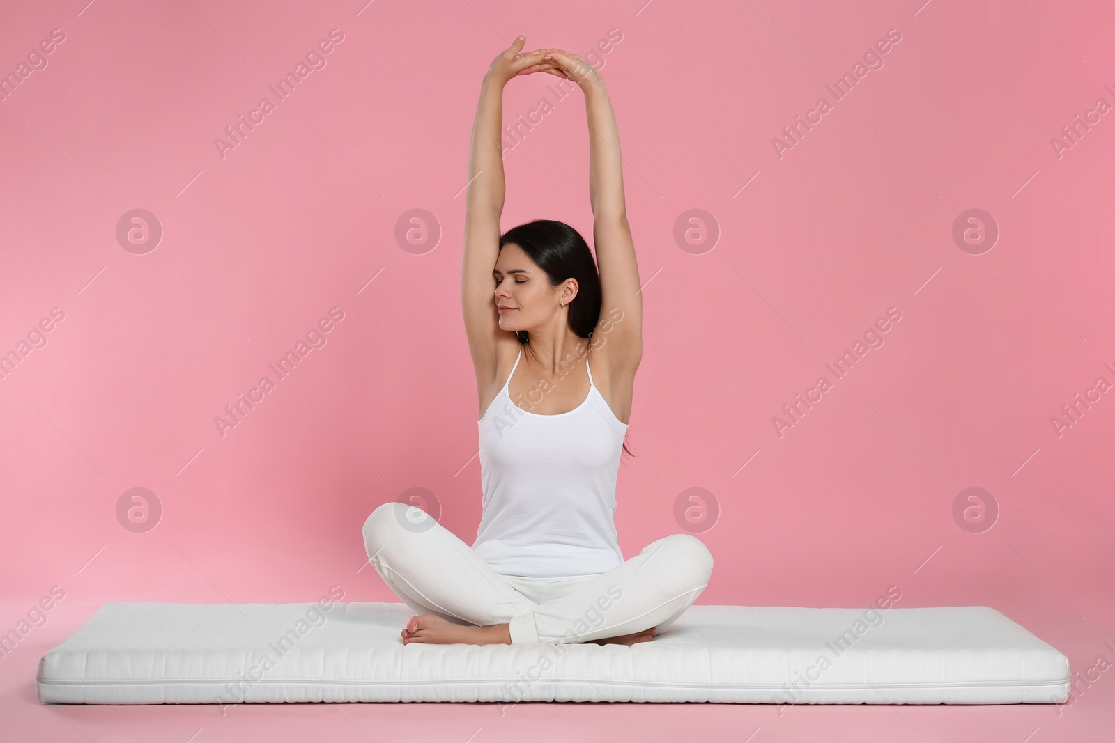 Photo of Young woman stretching on soft mattress against pink background