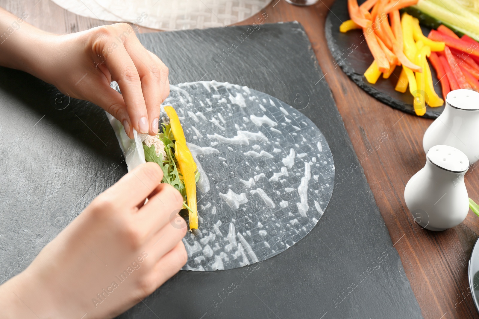 Photo of Woman making rice paper roll at wooden table, closeup