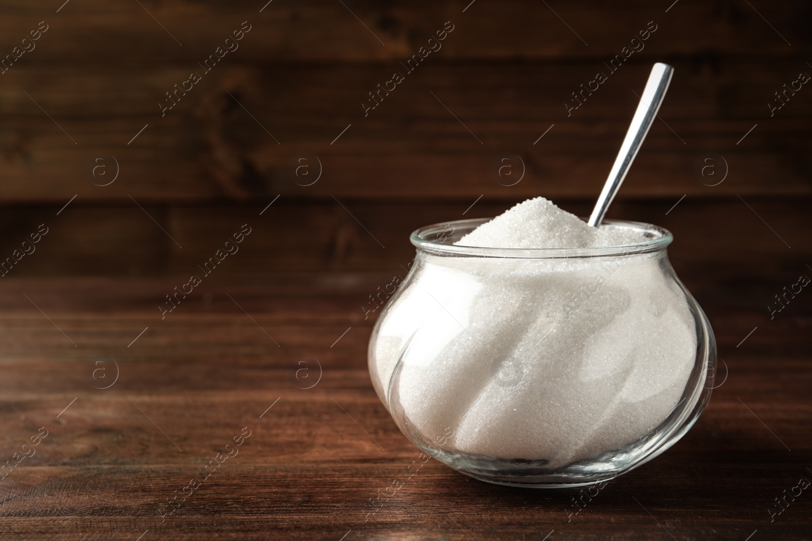 Photo of Glass bowl with sugar and spoon on wooden table. Space for text