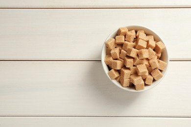 Brown sugar cubes on white wooden table, top view. Space for text