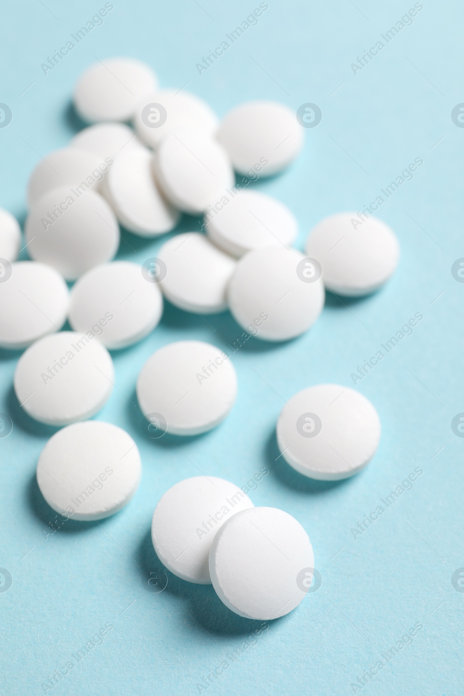 Photo of Many white pills on light blue background, closeup