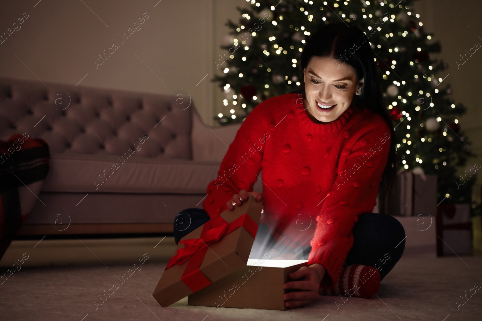 Photo of Beautiful woman opening gift box in living room. Christmas celebration