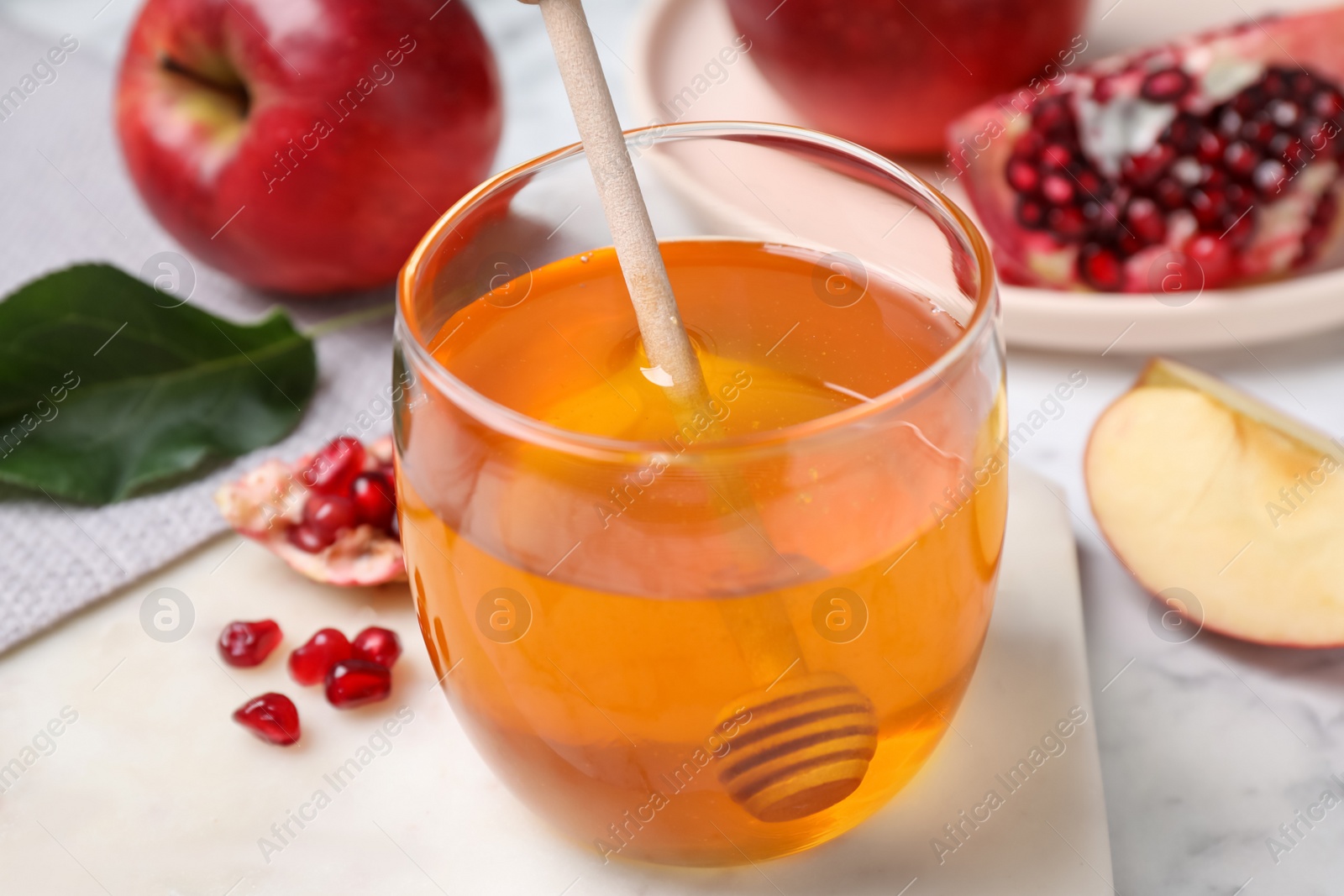 Photo of Honey, apples and pomegranate seeds on white marble table, closeup. Rosh Hashanah holiday