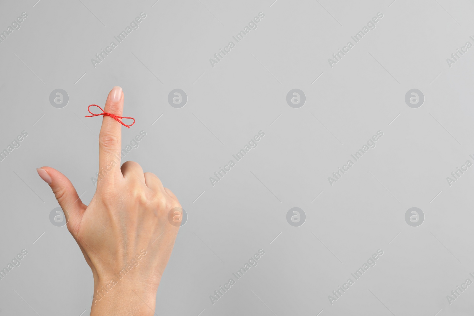 Photo of Woman showing index finger with tied red bow as reminder on light grey background, closeup. Space for text