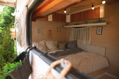 Photo of Stylish interior with comfortable bed and pillows in modern trailer, view from outside. Camping vacation