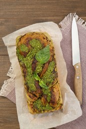 Freshly baked pesto bread with basil and knife on wooden table, flat lay