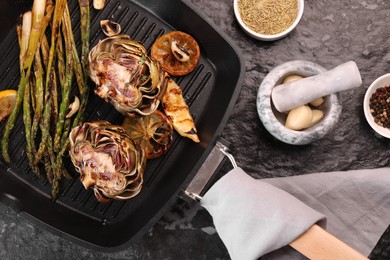 Tasty grilled artichoke and asparagus on dark textured table, flat lay