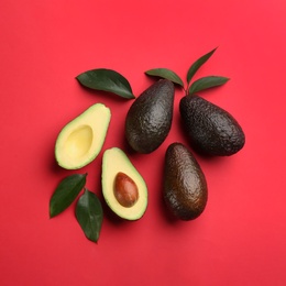 Photo of Whole and cut ripe avocadoes with green leaves on red background, flat lay