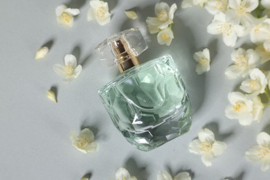 Photo of Aromatic perfume in bottle and beautiful jasmine flowers on grey background, flat lay