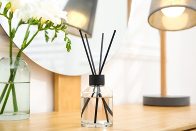Photo of Aromatic reed air freshener and flowers on wooden table in room