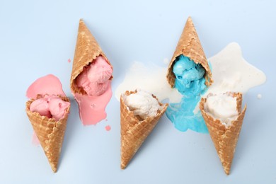 Melted ice cream in wafer cones on light blue background, flat lay