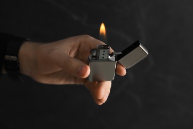 Photo of Man holding lighter with burning flame on dark background, closeup