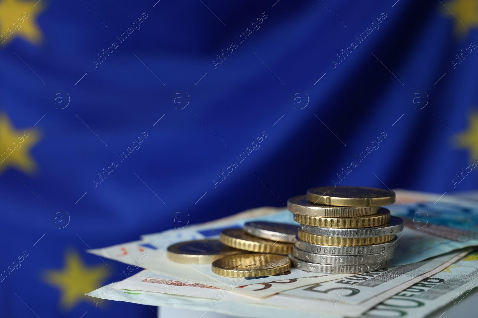 Photo of Coins and banknotes on table against European Union flag, closeup. Space for text