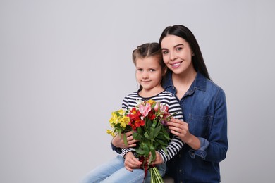 Photo of Happy woman with her cute daughter and bouquet of beautiful flowers on light grey background, space for text. Mother's day celebration
