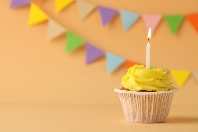 Tasty birthday cupcake with candle on orange table against party flags. Space for text
