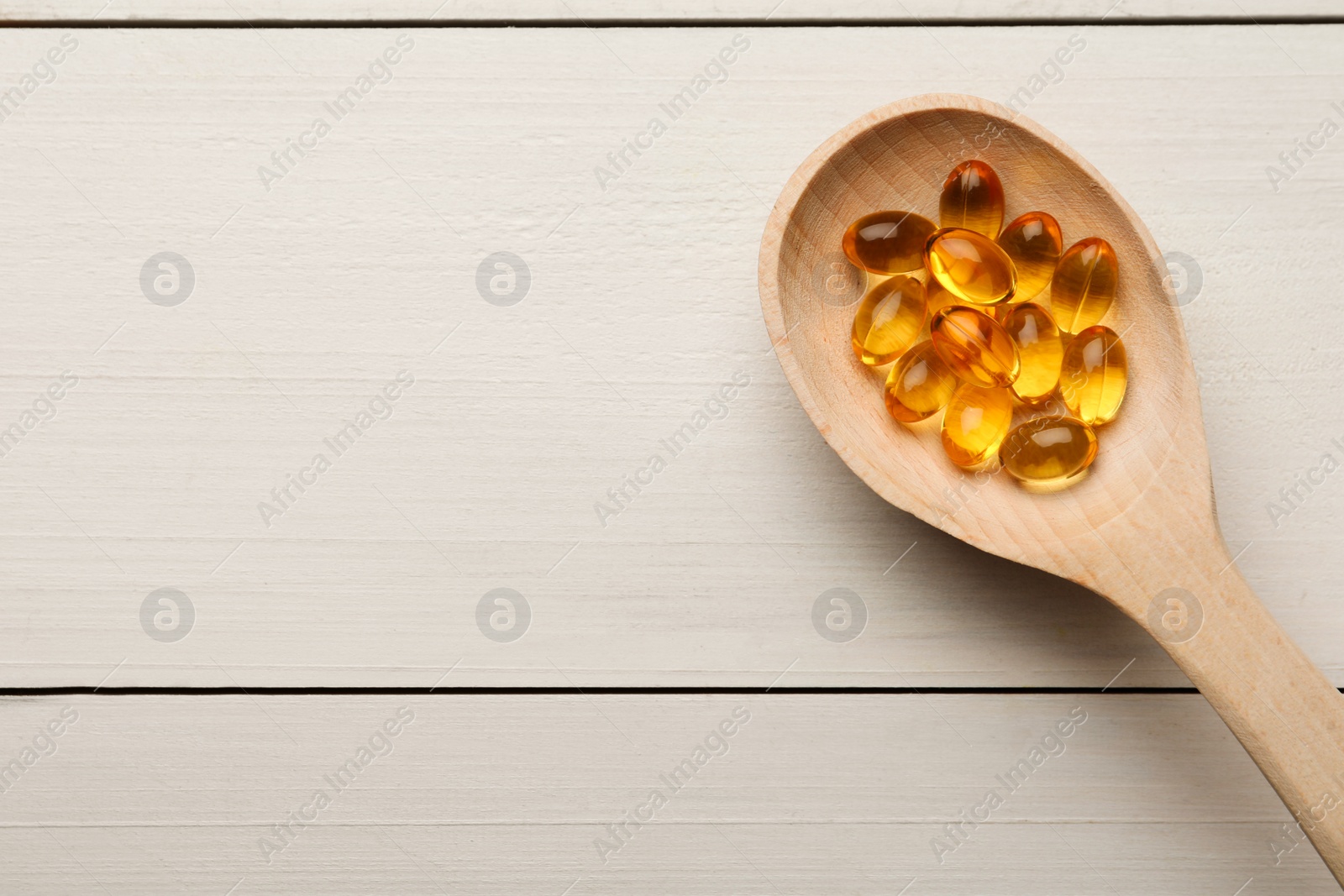 Photo of Spoon with dietary supplement capsules on white wooden table, top view. Space for text