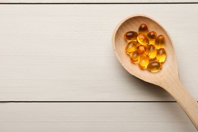 Photo of Spoon with dietary supplement capsules on white wooden table, top view. Space for text