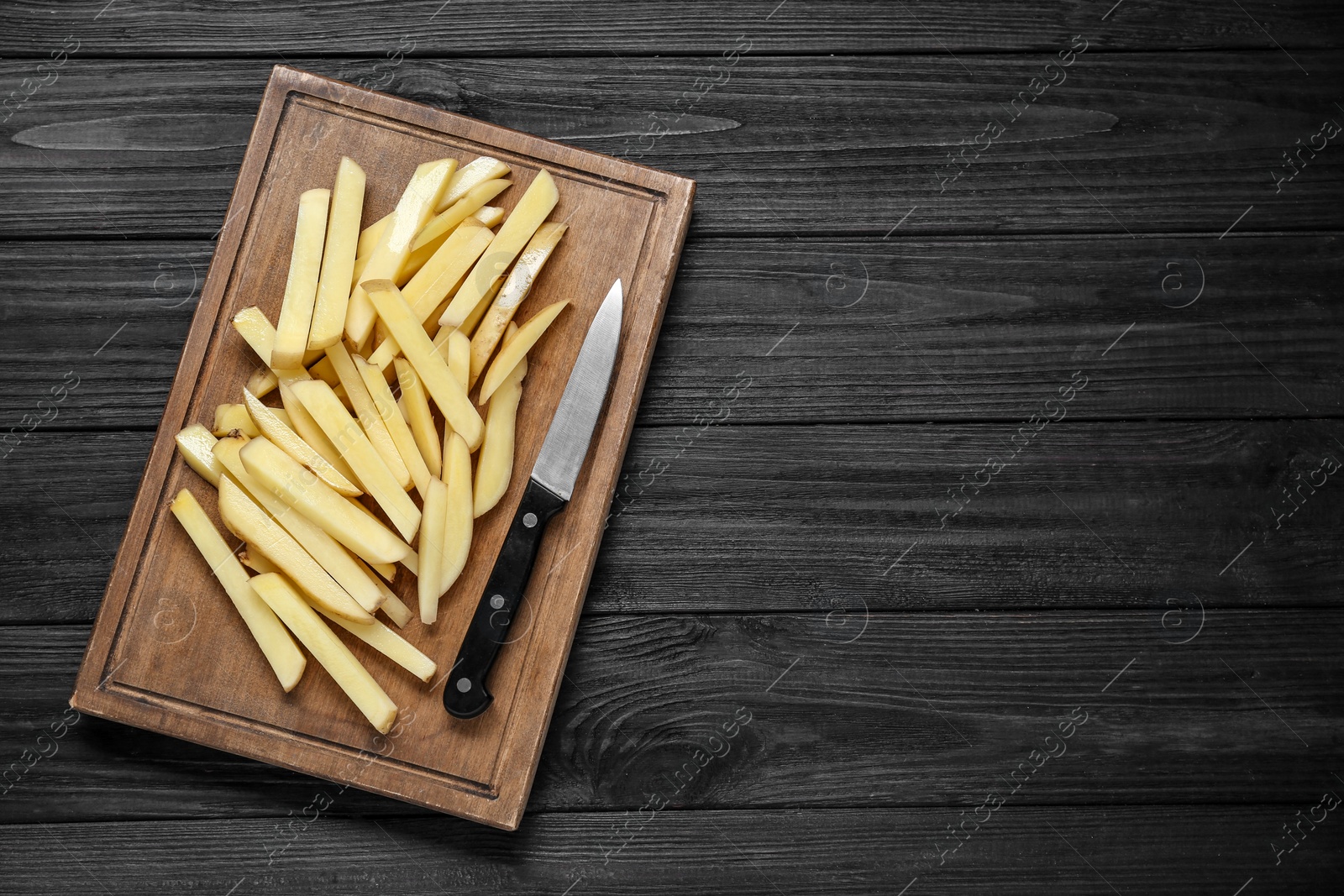 Photo of Cut raw potatoes on black wooden table, top view. Space for text