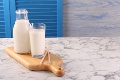 Glassware with tasty milk and straws on white marble table, space for text