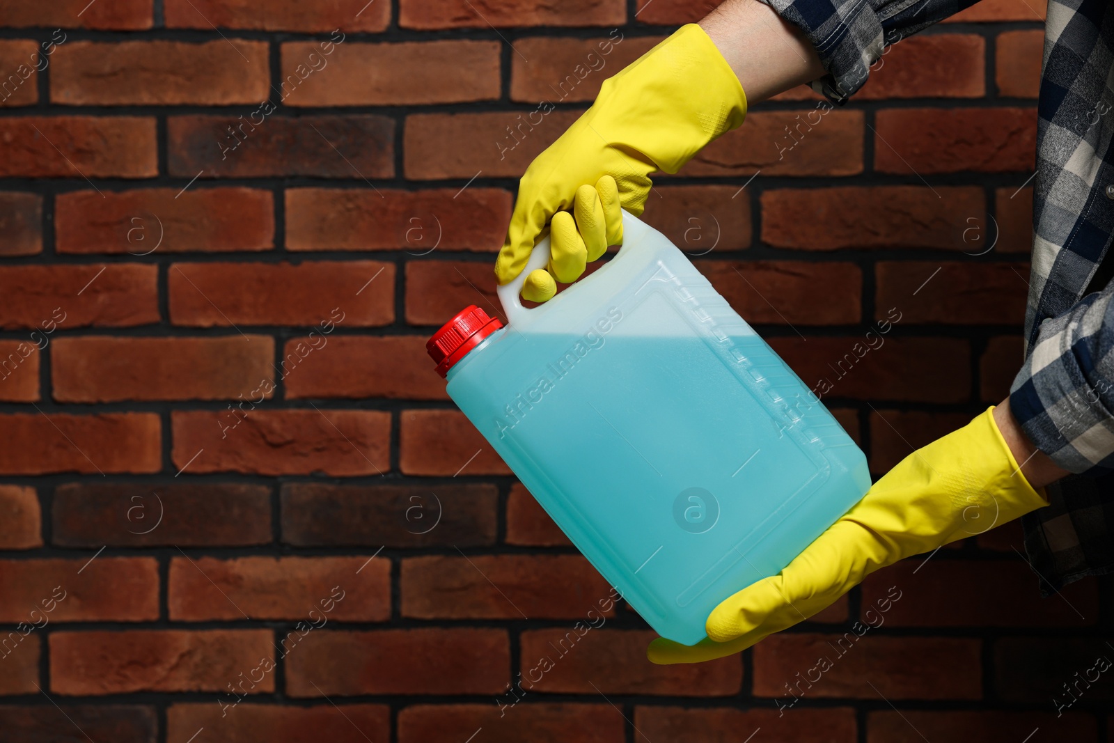 Photo of Man in rubber gloves holding canister with blue liquid near brick wall, closeup. Space for text