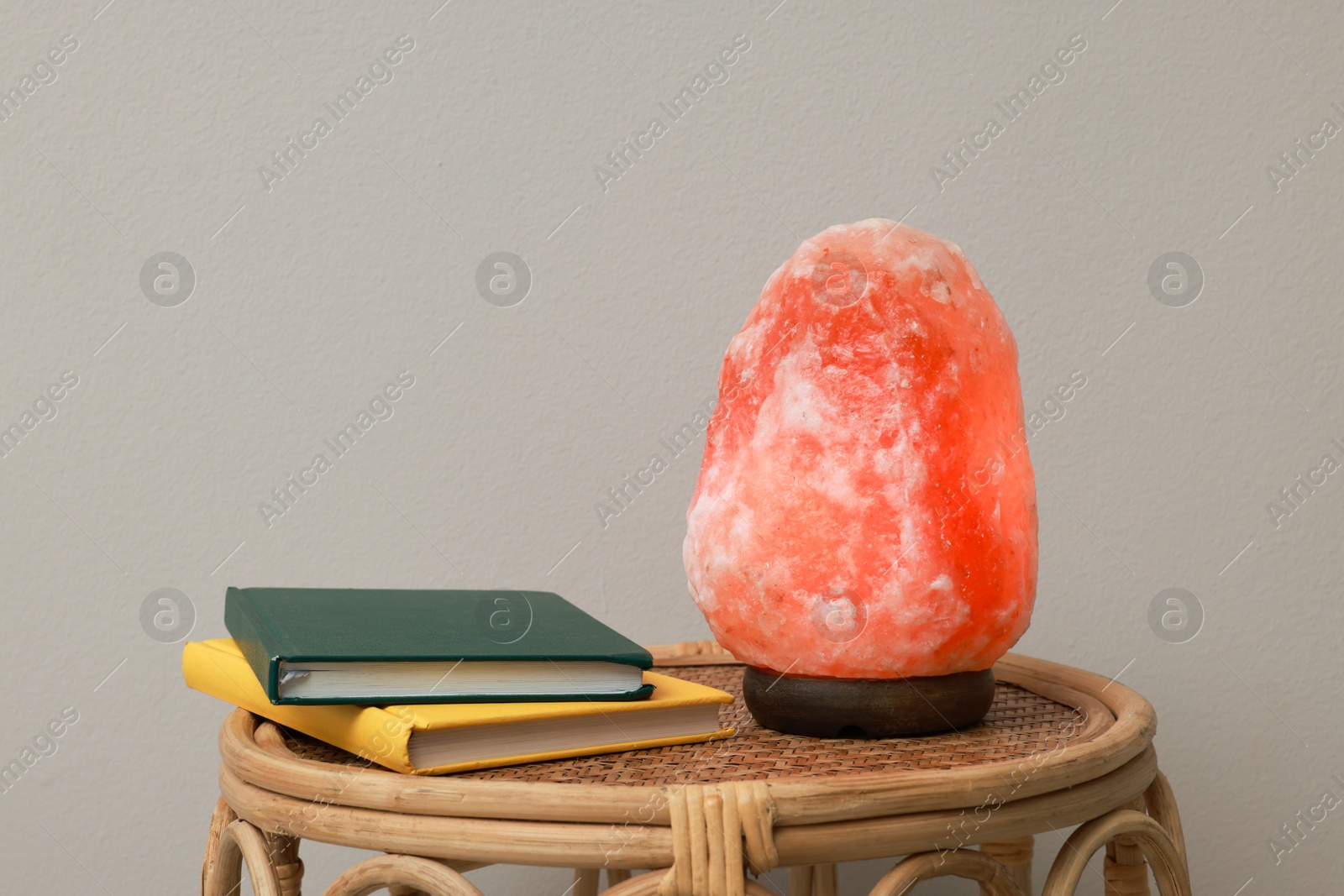 Photo of Beautiful Himalayan salt lamp and books on wicker table against grey background, space for text