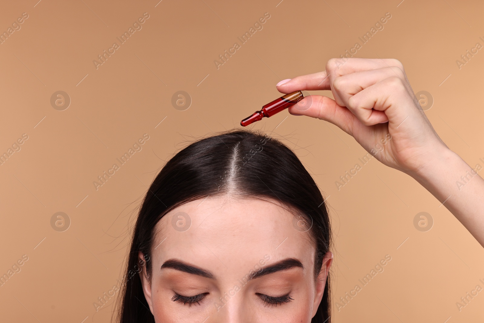 Photo of Beautiful young woman using ampoule for hair treatment on beige background, closeup