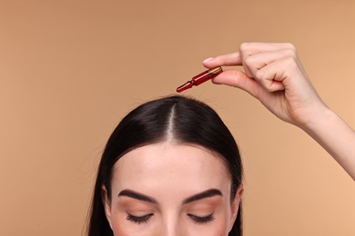 Beautiful young woman using ampoule for hair treatment on beige background, closeup