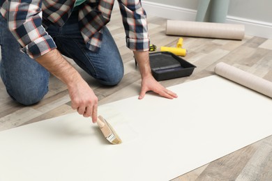 Photo of Man applying glue onto wall paper on floor, closeup