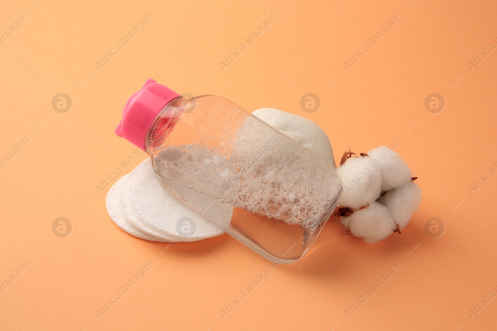 Photo of Composition with makeup remover and cotton flower on pale orange background