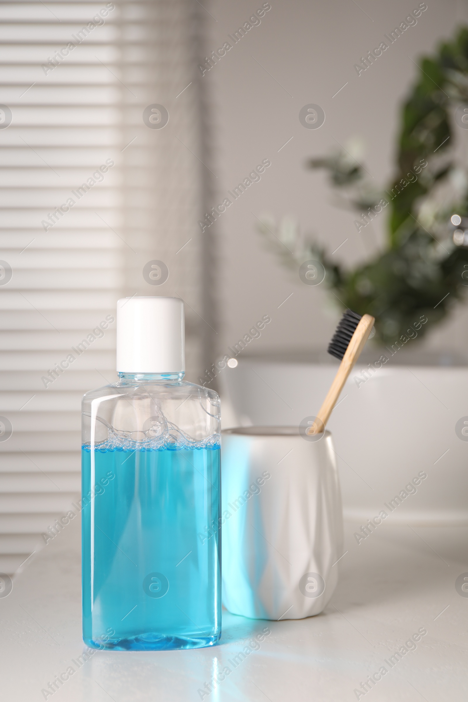 Photo of Bottle of mouthwash and toothbrush on white countertop in bathroom