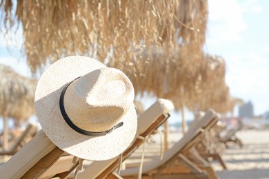 Photo of Stylish straw hat on wooden sunbed at beach, space for text